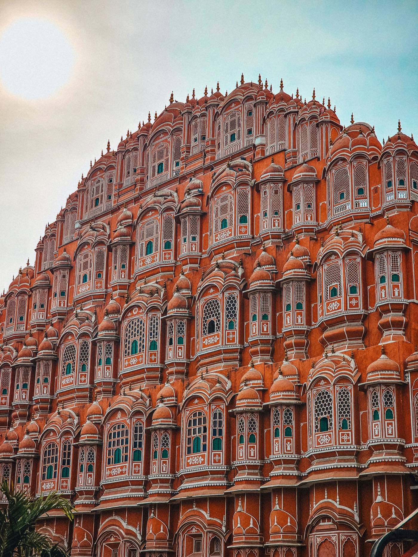 The pink sandstone facade of Hawa Mahal in Jaipur, five storeys of small latticed windows and domed balconies rising in tiers.
