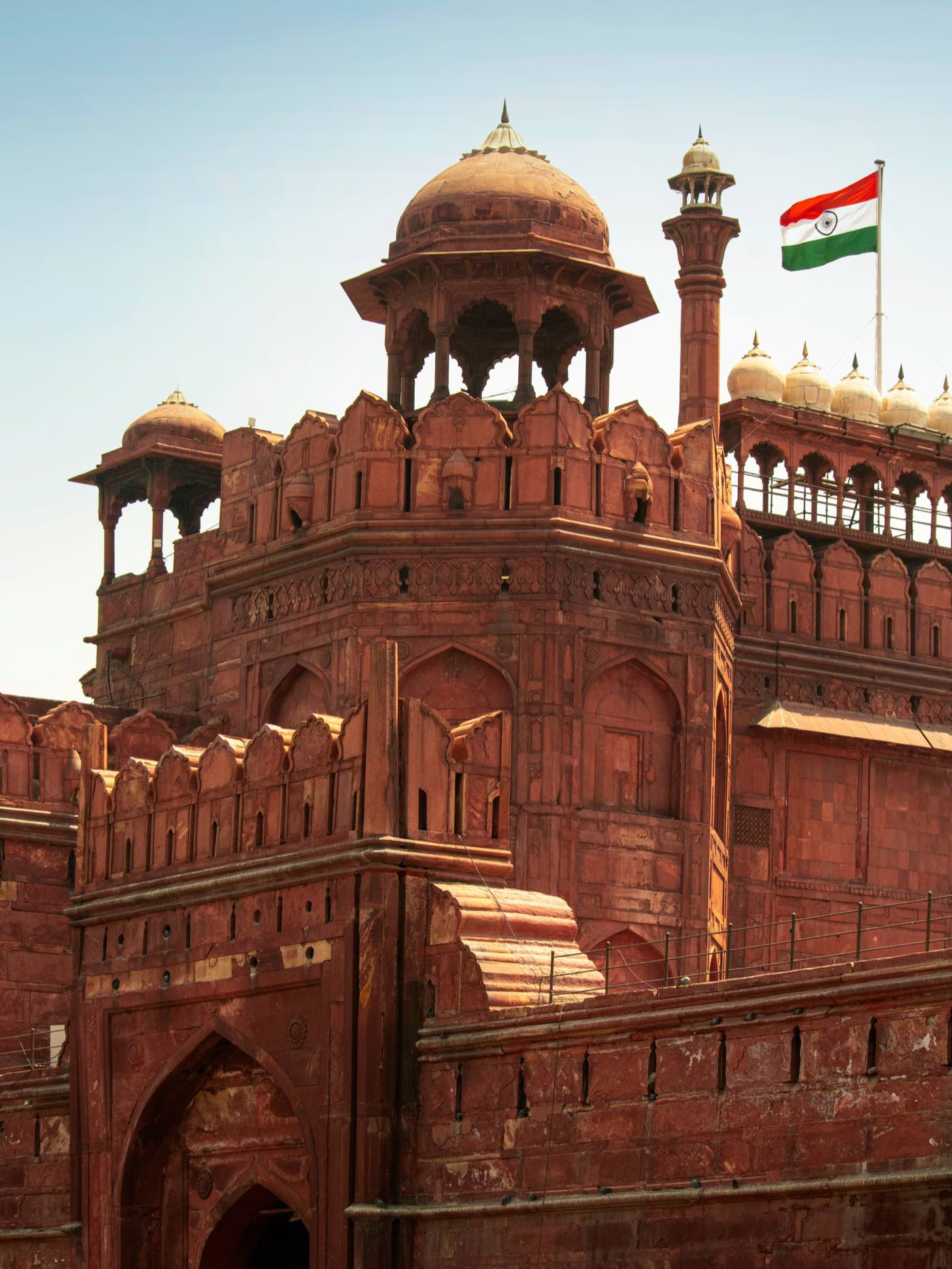 The red sandstone gatehouse of the Red Fort in Delhi, with domed pavilions along its walls and the Indian flag flying above.